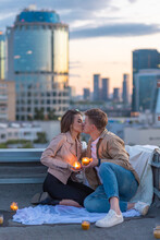 Beautiful Young Loving Couple On A Surprise Date On A Saint Valentine's Day On A Rooftop. Romantic Picnic With Candles. Newlyweds. Panoramic View, Urban Cityscape With Skyscrapers On Background
