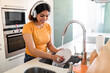 © Prostock-studio - Smiling Arab Housewife Washing Dishes In Kitchen And Listening Music In Headphones