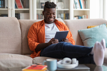 Wall Mural - Smiling african american guy using digital pad at home