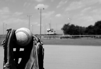 Sticker - Baseball glove with ball, sports field blurred background in black and white.