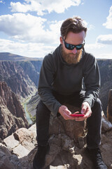 man with sunglasses in a grey sweatshirt looking at a cellphone - Black Canyon of the Gunnison National Park - Colorado - landscape - remote work