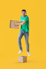 Wall Mural - Young volunteer with cardboard boxes jumping on yellow background