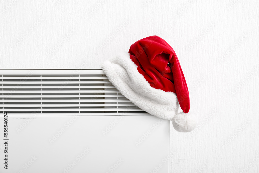 Santa hat on electric radiator near light wall, closeup