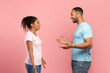 © Prostock-studio - Side view of excited african american friends man and woman spreading hands and talking, pink background