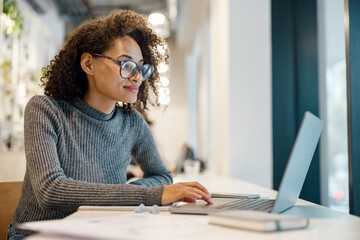 Wall Mural - Smiling afro american woman student studying online while sitting in cozy cafe