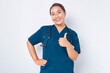 © Bangun Stock Photo - Smiling young Asian woman nurse wearing blue uniform with a stethoscope has all under control and shows thumbs-up in approval isolated on white background. Healthcare medicine concept