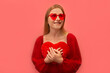 Excited dreaming happy young woman holding red toy heart close to chest, wearing red dress with trendy heart glasses and looking up isolated on pink background.

St Valentines Day or love concept.