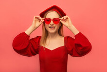 Happy Winking Stylish Young Woman Showing Tip Of Tongue, Closing One Eye And Looking At Camera Isolated On Pink Background.

Blonde Girl Wearing Red Dress With Beret And Holding Heart Shaped Glasses.