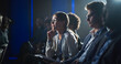 © Gorodenkoff - Young Woman Sitting in a Crowded Audience at a Business Conference. Female Attendee Writing Down Important Bullet Points into a Notebook. Keynote Speech in Auditorium with Successful Businesspeople.