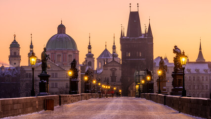 Wall Mural - Charles Bridge covered in snow with shining lanterns in Prague during golden hour in the winter morning.