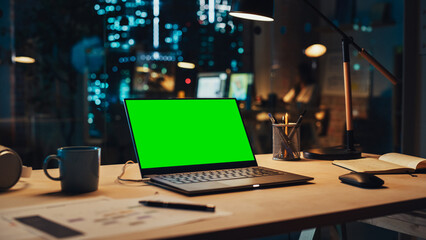 Poster - Laptop Computer Display with Mock Up Green Screen on a Table in Agency Office in the Evening. Chroma Key Monitor with Professional Working in the Background.