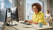 © Gorodenkoff - Portrait of Biracial Creative Young Woman Working on a Computer in Bright Busy Office During Day. Female Recruiter Smiles While Checking Job Candidates. People Working in the Background.