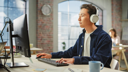 Aufkleber - Portrait of Asian Creative Man Using Computer and Headphones in Bright Modern Office. Male Data Analyst Developing Database While Listening to Music.