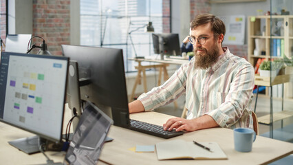 Poster - Portrait of Creative Bearded White Man with Glasses Focused While Using Computer in Bright Spacious Office. Marketing Manager Building a New Strategy.