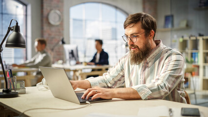 Poster - Portrait of Caucasian Young Man Working on a Laptop in a Spacious Bright Office. Male Sales Representative Negotiating Contracts with Clients. People Working on Computers in the Background.