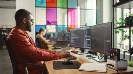 Fototapete - African American Man Coding on Desktop Computer with Professional Multiple Monitors Setup in Creative Office. Male Software Engineer Developing Mobile Application for Innovative Start-Up Company.