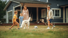 Joyful Young Couple With Kids, Playing Ball With An Energetic White Golden Retriever. Cheerful People Playing Football With Pet Dog On A Lawn In Their Front Yard In Front Of The House.