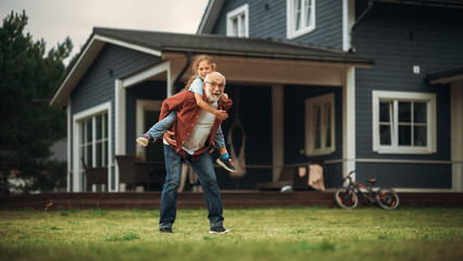 Wall Mural - Happy Granddad Enjoying Time Outdoors with His Grandchild, Playing with Energetic Young Girl. Joyful Grandpa Giving a Piggyback Ride on a Lawn in Front of the House.