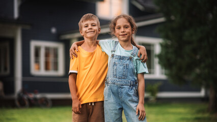 Wall Mural - Young Happy Brother and Sister Standing in Front of a Country House, Embracing Each Other, Looking at Camera and Smiling. Two Kids Enjoying Childhood and Friendship.