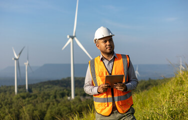 Engineer India man working with tablet at windmill farm Generating electricity clean energy. Wind turbine farm generator by alternative green energy. Asian engineer checking control electric power