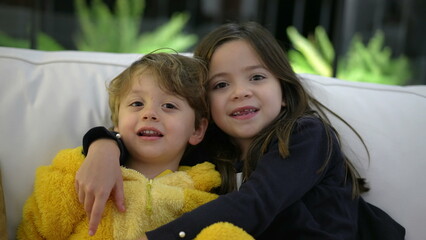 Happy little siblings posing for camera. Child sister embracing small baby brother kissing on cheek. Family love and affection