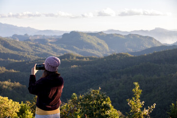 Wall Mural - woman taking photo of beautiful mountain landscape with mobile phone. Girl make a photo with her cell phone from the top of the mountain. Take phone photo. Hiker sit at edge for taking selfie picture