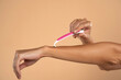 © vladimirfloyd - A woman shaves her arms with a disposable pink razor on a beige background
