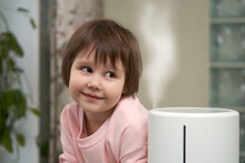 The Face Of A Smiling Little Girl Next To The Humidifier In The Room.