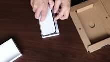 Close up of hands of man taking out brand new smartphone from box and slowly removing film screen protector.
