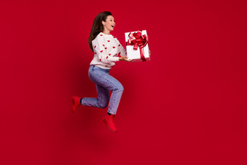 Sticker - Full length photo of pretty cute lady wear white sweater holding gift jumping high running empty space isolated red color background