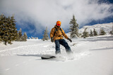 Young athletic snowboarder in bright yellow coat riding down on splitboard splashing snow