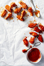 Chicken Wings Coated With Two Different Sauces On White Parchment Paper With Spoon And Brush