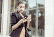 © splitov27 - Young business woman using snmartphone and drinking coffee on the go outdoors