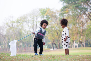 Two little children playing and doing volunteer charity environment outdoor in the park. Child girl and boy collecting trash into a bag outdoors