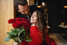 Bearded Man In Suit Holding Bouquet Of Red Roses Near Joyful Girlfriend On Valentines Day