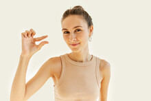 Too Small. Happy Woman With Hair Bun Showing Little Tiny Small Size Gesture With Funny Sarcastic Facial Expression, Smiling Mockingly, Isolated On White Studio Background. Body Language