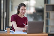 © Songsak C - Concentrated at work. Confident young woman in smart casual wear working on a laptop while sitting near a window in a creative office or cafe.