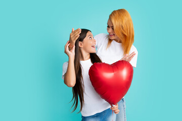 Poster - Mothers day. Smiling mother and daughter holding love heart balloon on blue background. Mommy with teenager daughter isolated on blue background studio portrait. Love family, parenthood concept.