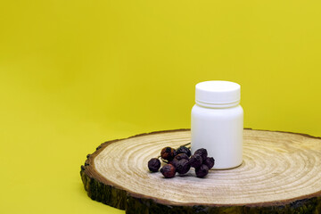 White plastic medical container with dry rosehip fruits on wooden board on yellow background, mockup. Blank Medicine bottle. Pharmacy business and treatment concept. Copy space. Close-up.