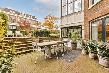 a patio area with chairs, tables and potted plants on the side of the house there is a brick wall in the background