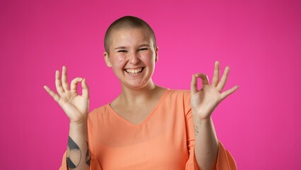 Portrait of young non binary gender fluid woman 20s giving okay gesture smiling happy isolated on pink background studio portrait