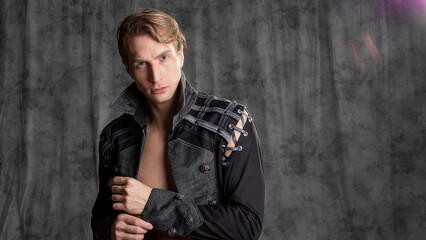 An attractive young man in a fantasy camisole, posing in the studio on a gray fabric background.