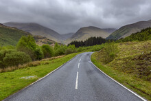 Winding Country Road And Hills With Overcast Sky At Glen Nevis Near Fort William In Scotland, United Kingdom
