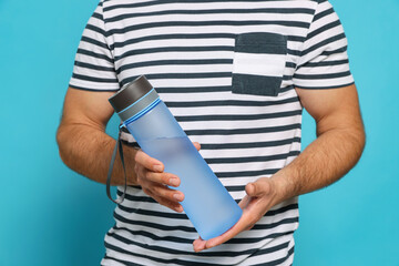 Wall Mural - Man holding transparent plastic bottle of water on light blue background, closeup