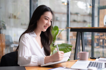 Smiling young asian businesswoman working on a laptop at her desk in a bright modern lofe office