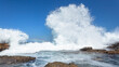 Wave Rocks Exploding White Water Power With Blue Sky Background Along Rocky Beach Coastline.