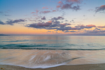 Sticker - calm turquoise ocean water under a olorful sunset sky with calm waves on the sandy shore