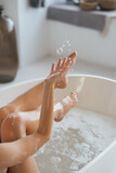 Fototapeta Kwiaty - Cropped view of young woman lying in foamy bath