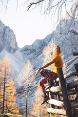 Canvas Print - Vertical photo of unrecognizable woman hiker sitting on a wooden fence somwhere in the autumn mountains