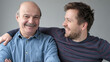 © RealPeopleStudio - Happy mature senior father and grown son standing together, hugging, looking at camera